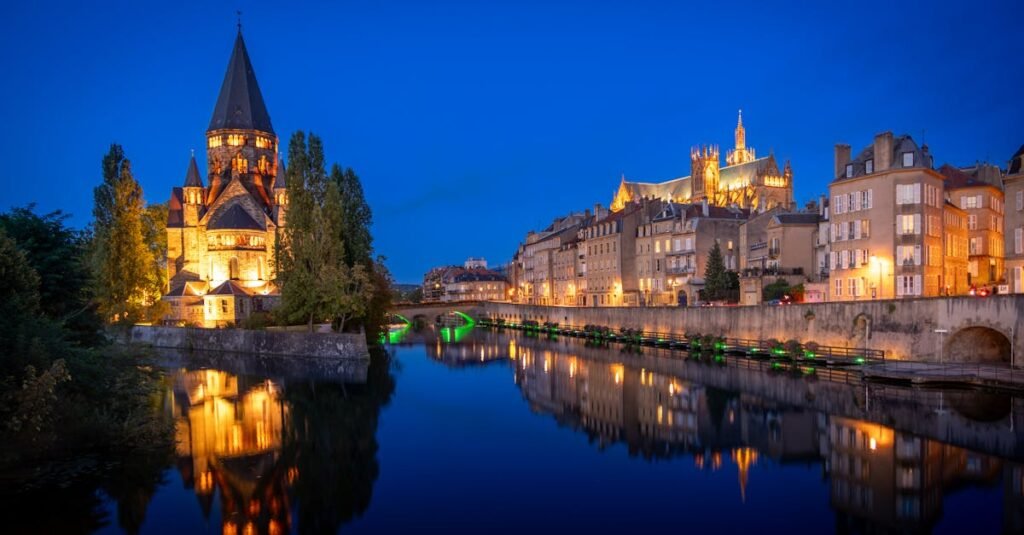 Captivating nighttime scene of Metz Cathedral and Moselle River reflecting city lights.